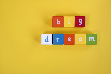 Words Big Dream made from colored wooden blocks. They are arranged in two rows. Painted cubes with letters on yellow background. Top view. Selective focus. Copy space.