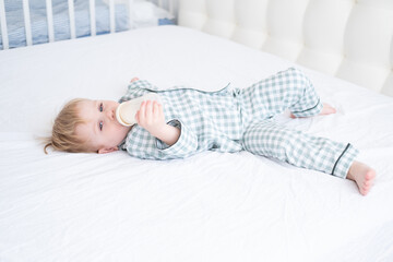 toddler baby boy in pajamas lie on bed drinking milk from bottles. Candid home childhood life