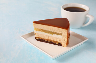 A piece of cake on a square plate with a cup of tea