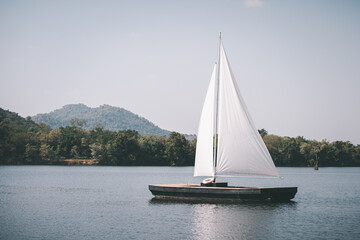 White sailing boat on a calm lake with nature and mountain background.
