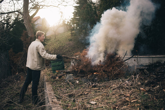 gardener man burning branch in fire pit during a summer revitalization of his garden