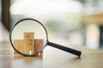 Hand holding magnifying glass and looking at house model, house selection, real estate concept.