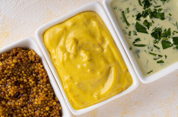 Three different mustard bowls on yellow cement background