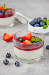 Italian dessert panna cotta in a glass with berry sauce, fresh strawberries and blueberries on top on a gray concrete background. Copy space.