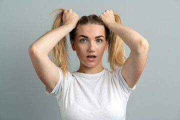Fototapeta premium Girl with a shocking look on a gray background. Beautiful, young girl holding two ponytails from her hair.