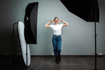 Girl makes gestures of victory and peace, she poses in a photo studio. The process of shooting in a...