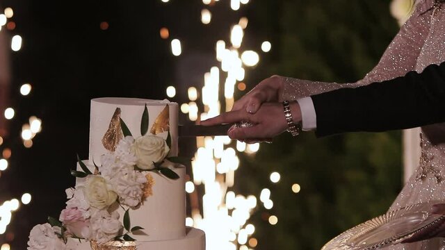 The bride and groom cut the wedding cake. Wedding cake with sparklers. Detail of wedding cake cutting by newlyweds. Cut the wedding cake
