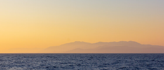Seascape with fog and mountains. Seascape at sunset. View from the sea to the mountains in the haze. Dramatic scenes and the beauty of nature