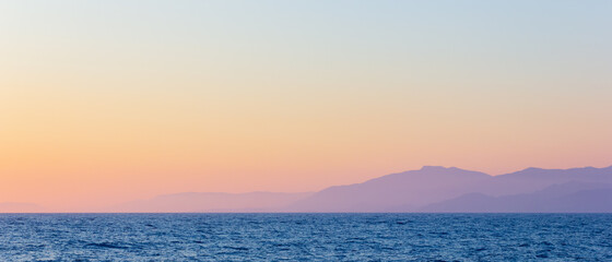 Fototapeta premium Seascape with fog and mountains. Seascape at sunset. View from the sea to the mountains in the haze. Dramatic scenes and the beauty of nature