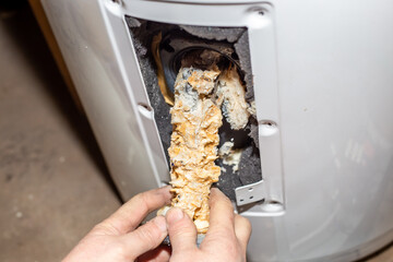 Repair and maintenance of boilers. The master plumber pulls out a tubular electric heater covered with lime scale from the hole in the boiler