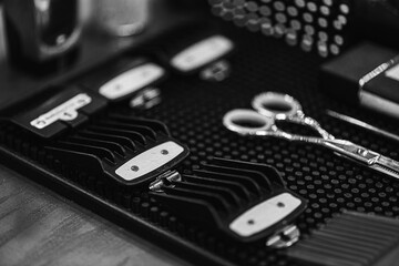 Black and white photo, selective focus, graininess, hairdressing items (nozzles for hair clippers, combs, scissors, hairdresser) are placed on the table before the haircut