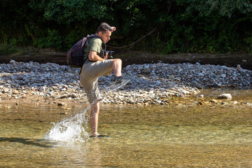 A young man dancing on the water on a sunny day, on a mountain river.