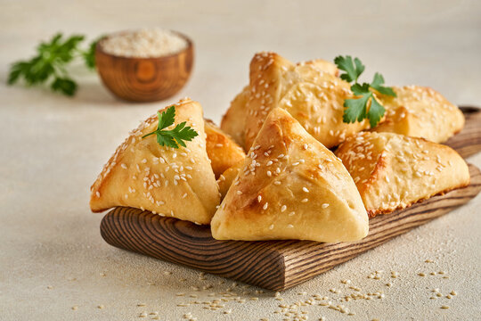 Fatayer pie samosa with white cheese and black sesame seeds on wooden board.