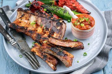 Modern style traditional barbecue pork loin ribs with vegetable and spicy tomato relish served as close-up on a Nordic design plate