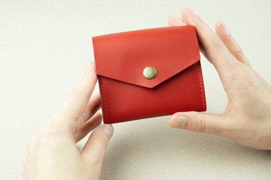 red leather wallet in female hands close-up on a gray background
