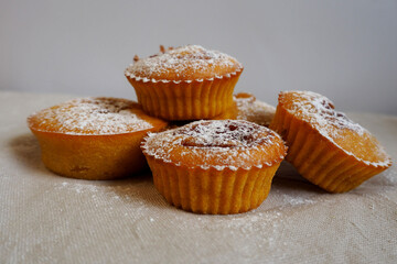 several pumpkin and carrot muffins with jam sprinkled with powdered sugar stand on a beige tablecloth against a gray wall side view . homemade cakes