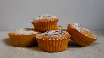 several pumpkin and carrot muffins with jam sprinkled with powdered sugar stand on a beige tablecloth against a gray wall side view 