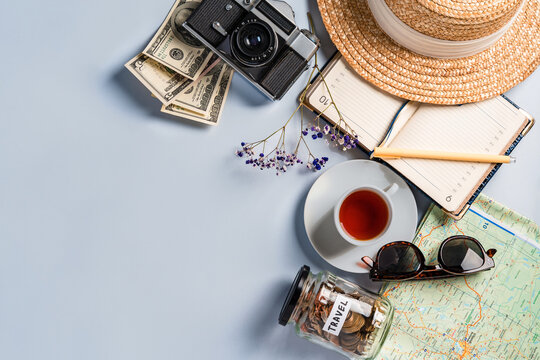 Top view of travel accessories when planning a trip: a camera, a notebook, a cup of tea. Space for text and a jar of coins