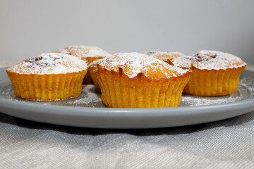 five round pumpkin muffins sprinkled with powdered sugar lie on a gray round plate on a gray tablecloth side view
