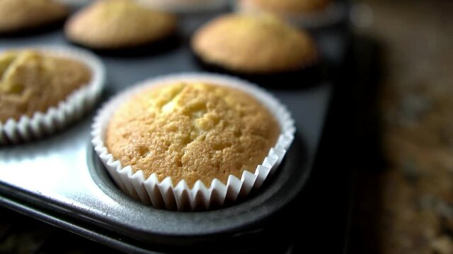 Slow motion closeup rotating motion around a baked vanilla or plain cupcake. Sitting in muffin tray on cooling rack in preparation of decorating. Home baking concept.
