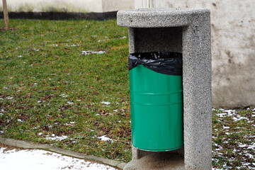 green metal garbage can stands in the park on a spring day side view