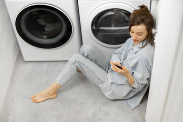 Relaxed woman with a smartphone in the laundry room