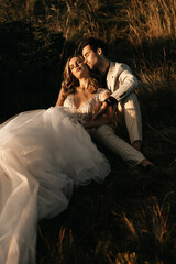 Beautiful young couple in love sit on the grass, bride in white dress, wedding couple
