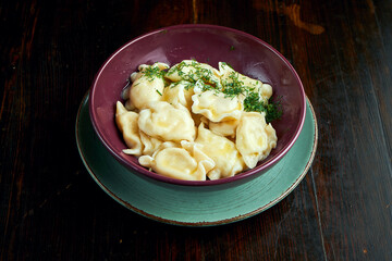 Traditional Ukrainian dumplings filled with salted coottage, served in a red bowl on a black background. Close up view on Pierogi or varenyky
