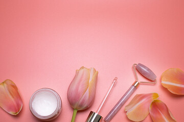 Beauty background with facial cosmetic products and petals, with free space for text. Modern spring skin care layout, top view, flat lay. Rose quartz face roller and petals on the pink background.