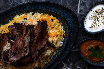 A plate of kabsa rice and grilled lamb and two small plates of Yogurt and hot sauce.