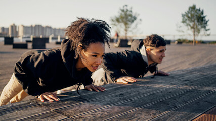 Sports couple shows a workout. Healthy lifestyle. Cardio training sports young people. Do push-ups on the embankment in the city center. Comfortable sportswear.