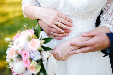 the bride holds a bouquet in her lowered hand, the groom hugs her waist from behind