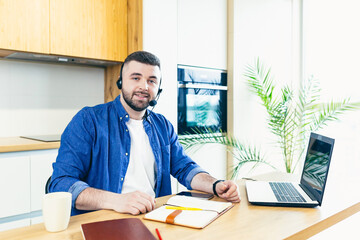 The man uses a headset with a microphone, makes an online video call, for consultations, with the help of a laptop, works at home