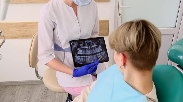 Doctor dentist shows problem areas on the x-ray for patient in stomatology office.