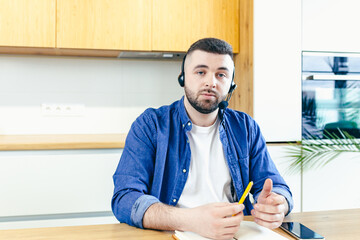 Male businessman looks at camera uses headset, and uses video call for online consultation,...