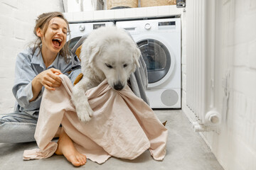 Woman with dog having fun in the laundry room at home