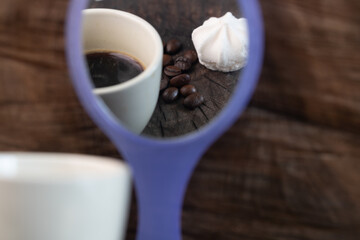 cup of coffee and beans on wooden table seen from mirror