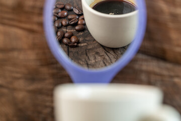 cup of coffee and beans on wooden table seen from mirror