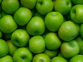 Background of bright ripe, green apples in full screen. The texture of greenhouse fruits in the window of the market, store.  Top view, close-up, food wallpaper. The concept of harvesting.