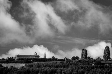 Fototapeta na wymiar Dramatic cloudy sky over the valley of San Quirico d'Orcia in Tuscany, Italy. Amazing landscape with church with single bell tower. Fairy-tale black and white picture