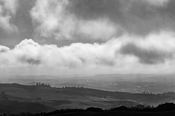 Dramatic cloudy sky over the valley of San Quirico d'Orcia in Tuscany, Italy. Amazing landscape with church with single bell tower. Fairy-tale black and white picture with dots, flying sky birds