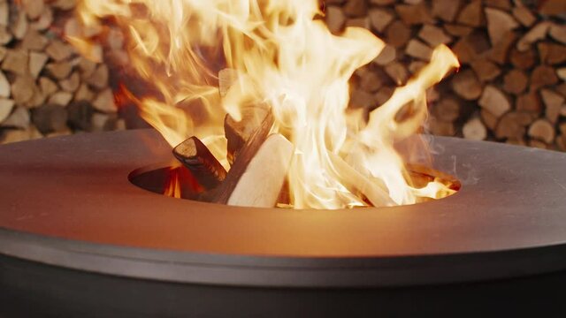 The young woman and her boyfriend are throwing firewood into a round metal designer brazier and light a fire.
