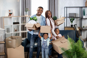 Fototapeta na wymiar Cheerful afro american family holding boxes at new flat