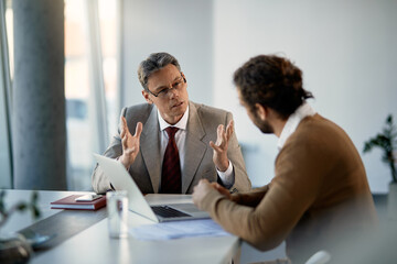 Mature businessman mentors newcomer and talks to him during meeting at company office.