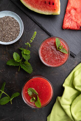 Watermelon juice with chia seeds and mint in glass on a black concrete background with green textile. Top view,  close up.