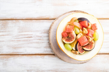 Vegetarian fruit salad of watermelon, grapes, figs, pear, orange, cashew on white wooden background. Top view, copy space.
