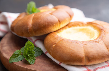 Sour cream bun with cup of coffee on a black concrete background. Side view, close up, selective focus.
