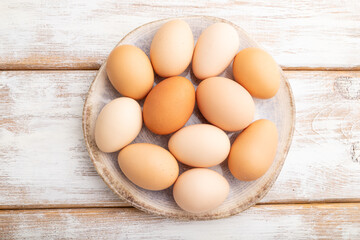 Pile of colored eggs on plate on a white wooden background. top view, close up.