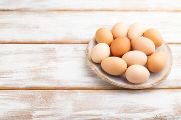 Pile of colored eggs on plate on a white wooden background. side view, copy space.