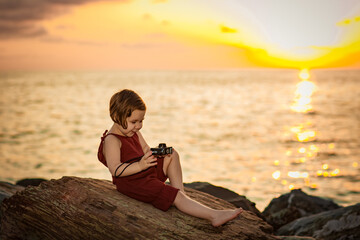 a little beautiful girl,on the beach,on a summer evening at a beautiful sunset, sits with a camera in her hands